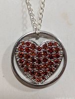 Close-up front view of silver necklace's heart-shaped pendant with red gemstones inside a circular frame.
