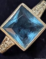 Close-up of silver ring with square blue genuine gemstone showing the faceted cut and bezel setting.