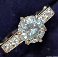 Close-up front view of silver ring showing large, round-cut moissanite center stone with accent stones on band.