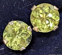Close-up of the front of the two round faceted peridot stone earrings showing their light green color and prong settings.