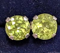 Close-up front view of two round faceted peridot stones set in silver prongs, showing color and cut.