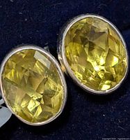 Close-up photo of pair of oval faceted peridot quartz earrings in silver setting, showing yellow-green gemstones and silver bezel.