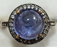 Close-up front view of silver ring with round cabochon tanzanite gemstone surrounded by small clear stones.