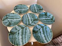 Top view of all 8 malachite green printed plates arranged on a round table showing consistent pattern style and gold rims