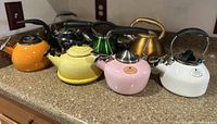 Photo of 7 Chantal whistling tea kettles in assorted colors on counter