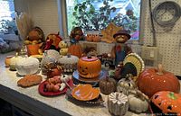 Wide angle showing the majority of ceramic holiday decorations arranged on a counter, including pumpkins, turkeys, leaves, and figurines.