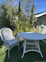 Full view of white resin wicker round dining table with matching chair on outdoor artificial grass.