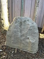 Front view of one faux boulder showing textured stone-like surface and gray color.
