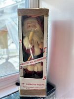 Front left view of the new in box Santa Claus animated figure showing the packaging, figure inside holding a liberty bell and candle.