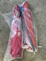Pair of red patio umbrellas wrapped in plastic, photographed on concrete surface to show lot contents.