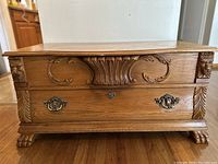 Front view of vintage cedar blanket chest showing hand carved floral and leaf designs, metal handles, keyhole, and claw feet.