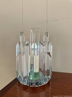 Front and side views of the prism-cut glass iridescent candlestick holder showing its geometric facets and a white candle held in the middle.