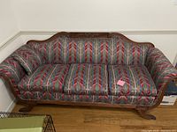 Full view of antique sofa showing carved wood frame and multicolored striped upholstery fabric.