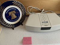 White Bose Wave Radio speaker with keypad next to blue and gold Bicentennial porcelain plate on stand