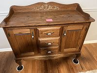 Front view of the solid oak buffet showing three central drawers and two cabinet doors with ornate carved detailing on top and base.