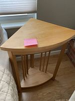 Maple corner table placed in a room corner showing the triangular top, 4 legs and curved lower shelf with vertical spindles.
