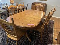 Full view of the solid oak dining table set with six matching chairs and extension leaf in place on a patterned rug.