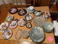 View of dog-themed plates depicting various dog breeds including Corgis and Collies, assorted clear glass bowls, crystal-like dish, and small ceramic dishes with blue designs.