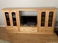 Full view of the maple entertainment center showing two side cabinets with glass doors and drawer, and central TV stand area with drawer and TV inside to illustrate size.