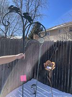 Two metal garden planter hangers with bunny silhouettes and decorative hooks, one with a flower-shaped planter holder attached, shown in snow-covered outdoor setting.
