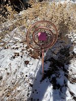 Garden ornament planted in snow-covered garden bed with dry plants in background, showing full structure and circular design.