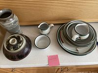 Overview of kitchen dishes including a ceramic vase, covered bowl, small pitcher and bowl, and a stack of nested plates and bowls with matching designs.