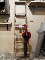 Wooden 6-step ladder standing upright with Toro red leaf blower hanging on the side.