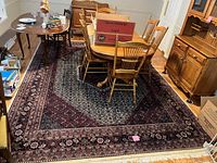 Full view of the large patterned area rug placed in a dining room under wooden dining table and chairs.