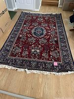 Full view of rectangular medium-sized area rug laid out on a wooden floor, showing overall pattern and fringe detail.