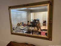 Full frontal shot of the large rectangular mirror mounted on wall reflecting dining room interior, showing gold ornate detailed frame and clear mirror surface.