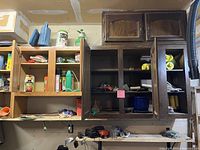 Photo showing two wood wall-mounted storage cabinets, one with doors closed and one partially open revealing miscellaneous small tools and items.
