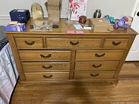 Front view of oak dresser showing the drawers, brass handles, and surface with various items on top.