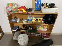 Photo of pine bookcase containing multiple decorative items, small stuffed toys, shoe polishes, books, and containers on shelves.