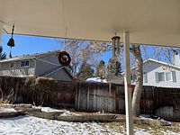 Photo showing the four windchimes hanging outdoors under a covered patio with houses and trees in the background in winter, some snow visible on ground