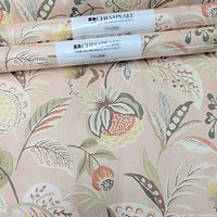 Close-up photo showing two rolled wallpaper with Chesapeake brand label and floral pattern in blush tone.