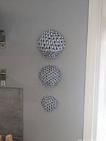 Photo of three blue and white ceramic fishnet shell wall decor pieces hanging vertically on a white wall.