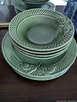 Stack of four green ceramic plates and four bowls, showing the bunny design on the rims with lattice texture.