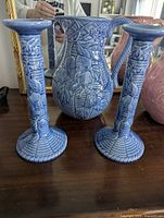 Pair of blue ceramic candle holders with intricate relief design and one blue ceramic jug with detailed floral and textured relief design.