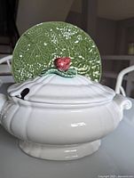 White soup tureen with strawberry-shaped lid handle in front of a green ceramic plate