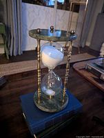 Front-side angle view of vintage hourglass showing the green marble base and top with brass spindle supports and white sand in glass bulb.