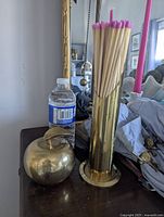 Both brass apple paperweight and cylindrical match holder displayed together with water bottle for scale.