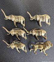 Top-down view of six brass napkin rings shaped as five elephants and one lion.