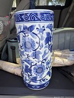 Photo showing the cylindrical chinoiserie blue and white ceramic vase with floral and bird design in natural lighting inside a vehicle.
