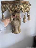 Hand holding the vintage gilded rope and tassel wall shelf corbel showing rope texture and tassel details under the top shelf.