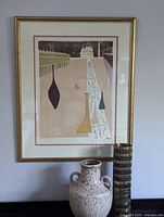 Front view of framed artwork on wall, gold-tone frame and off-white mat with red border