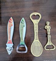 Four vintage bottle openers including two fish-shaped and two brass ones, shown on a wooden surface.