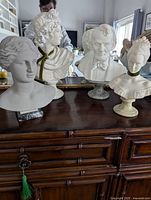 Four white busts displayed on wooden sideboard, front view