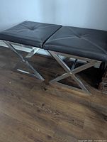 Two benches side by side, showcasing the black cushioned tops and chrome X-frame bases against a hardwood floor.