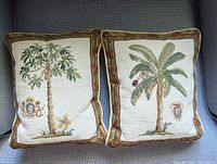 Front view of both petite needlepoint pillows showing palm tree and crest designs.