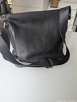 Full view of black leather messenger bag showing the front flap and shoulder strap.